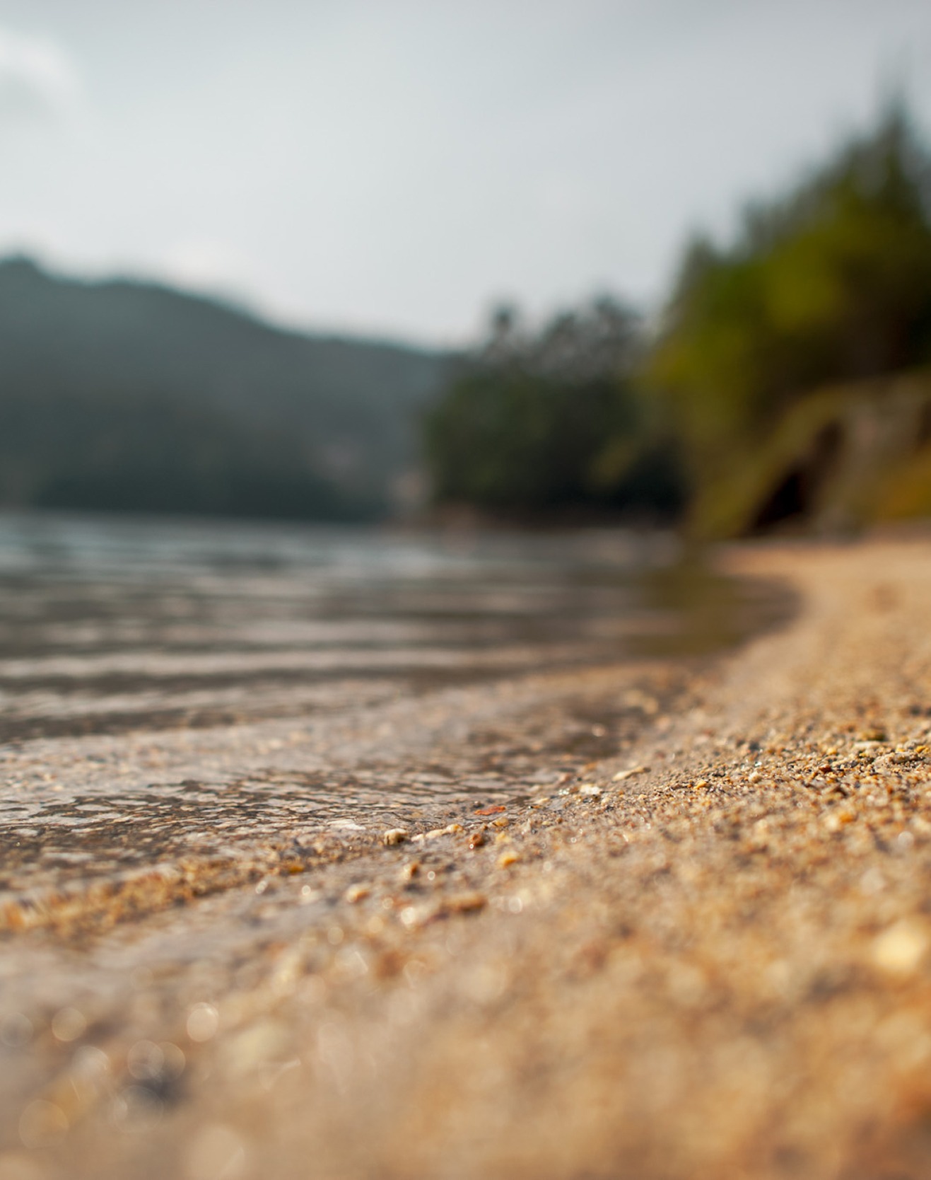 Close-up of sandy lakeshore with gentle water and blurred hills in the background