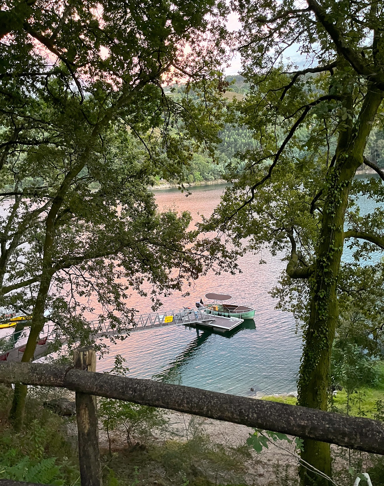 View through trees toward a wooden pier extending into the lake at Runas Carqueijais in Gerês